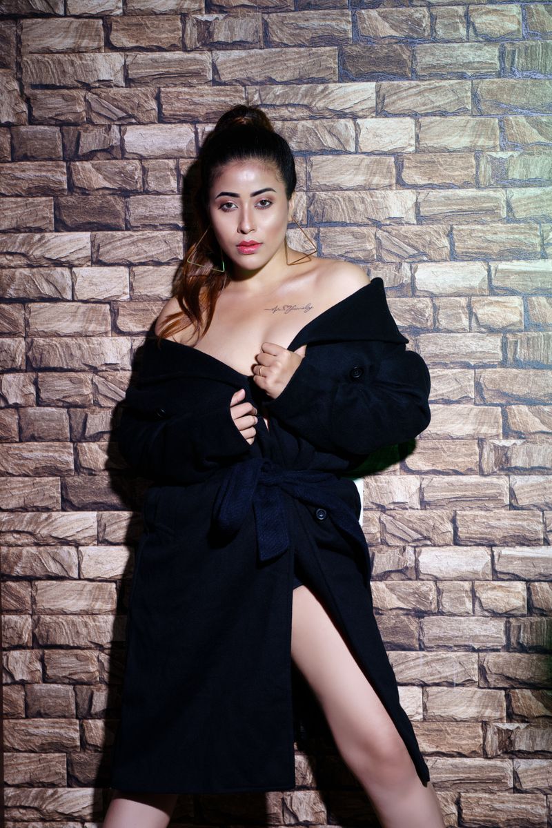 Striking portrait of a woman in a fashionable black coat posing against a brick wall.