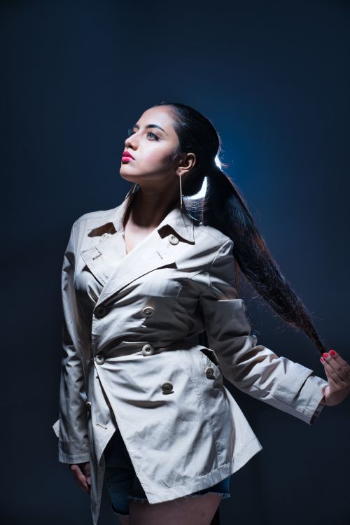 Free Elegant studio portrait of a stylish woman in a trench coat, striking a confident pose against a dark background. Stock Photo