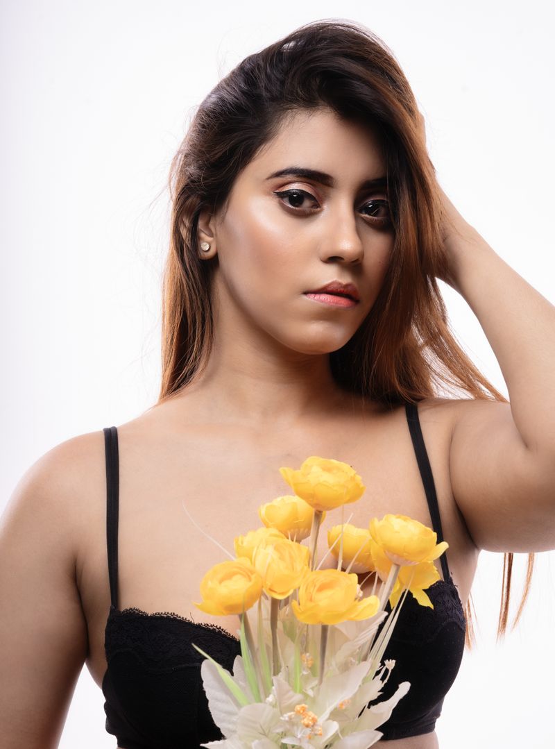 Stunning portrait of a woman with brown hair holding yellow flowers against a white background.