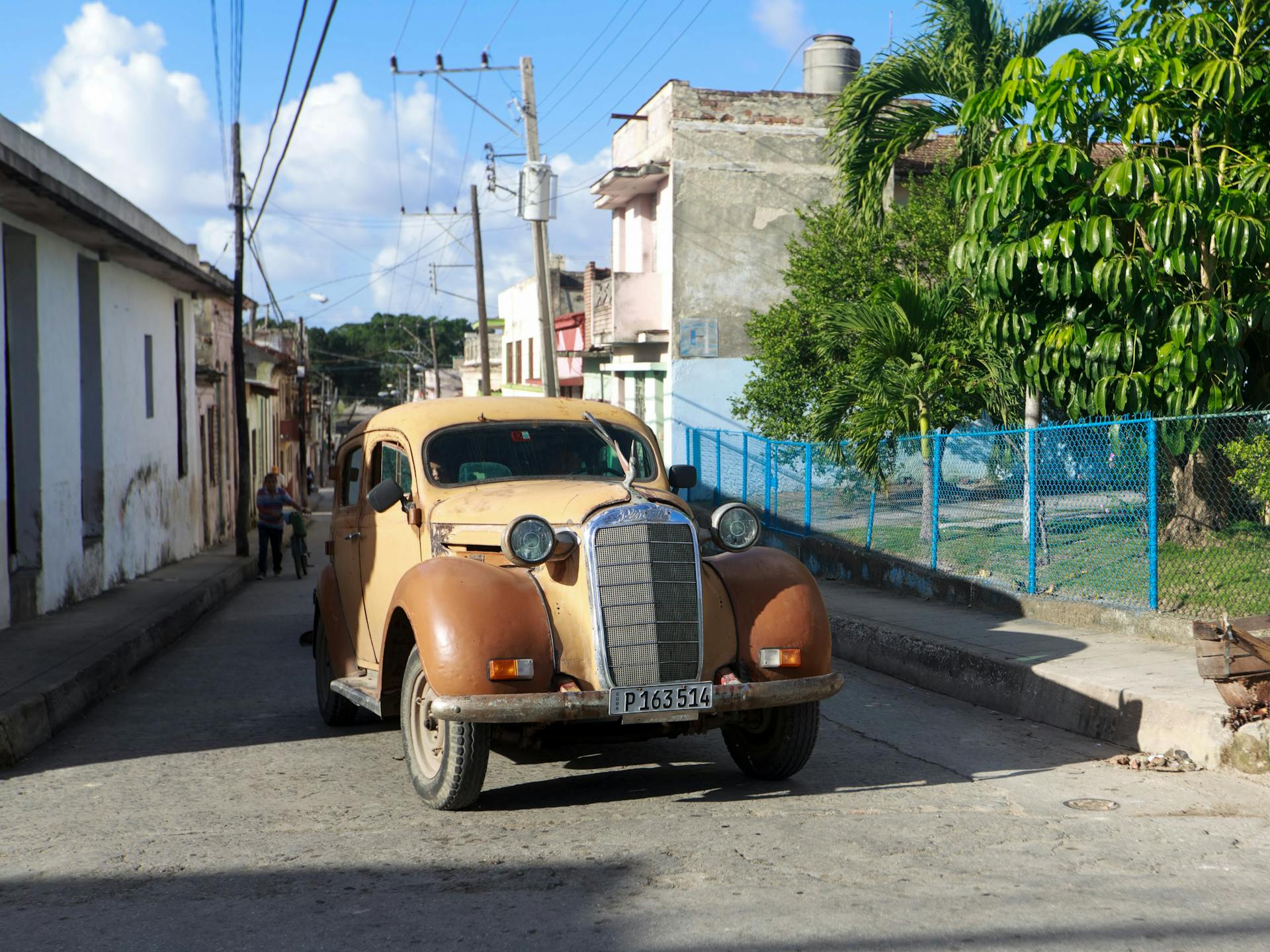 A classic vintage car parked on a sunny street, surrounded by colorful urban scenery.