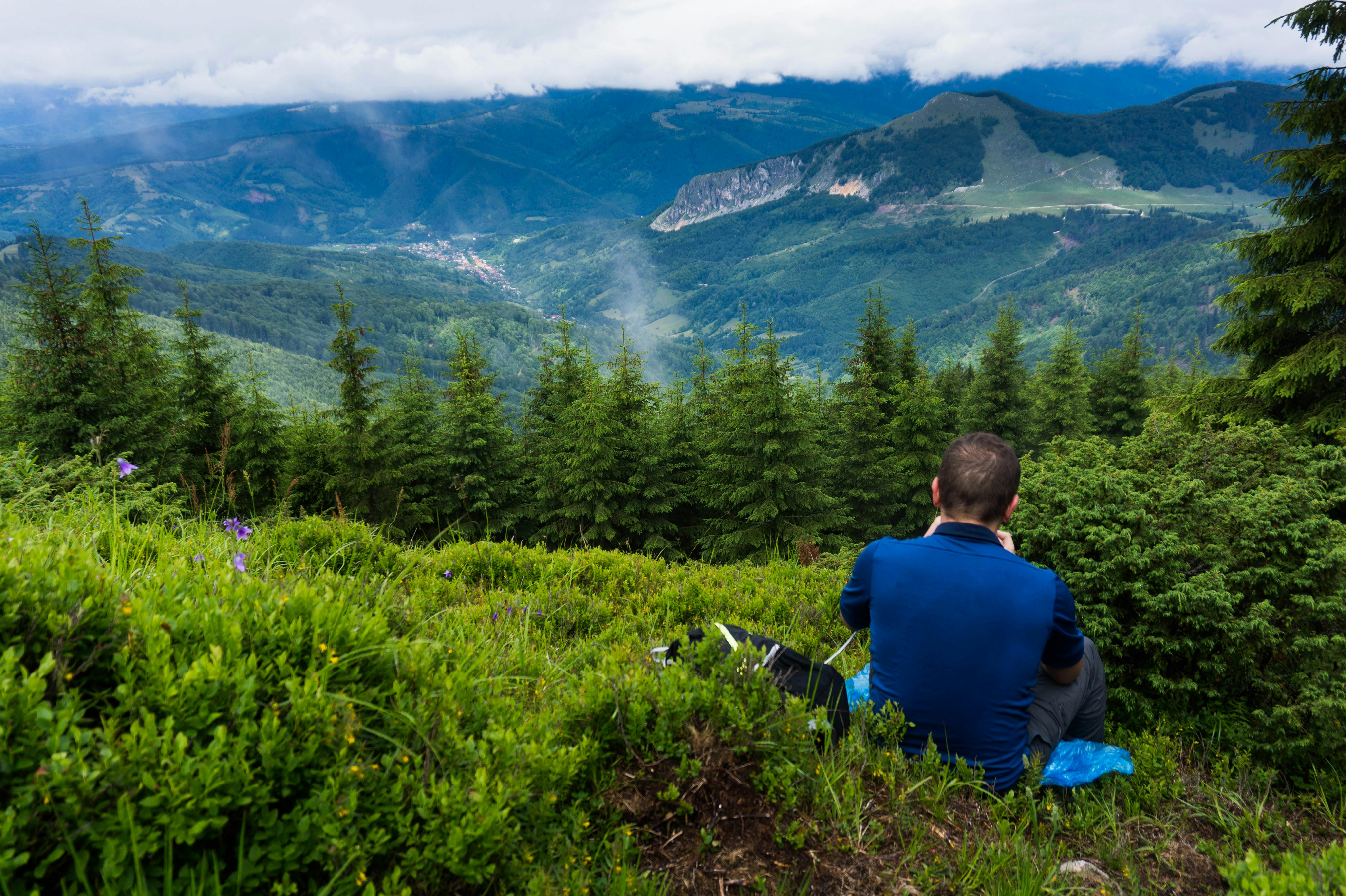 一名男子坐在多云的天空下，俯瞰着郁郁葱葱的青山，捕捉大自然的美丽