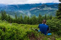 一名男子坐在多云的天空下，俯瞰着郁郁葱葱的青山，捕捉大自然的美丽