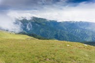 在多云的天空下，雾蒙蒙的山脉和郁郁葱葱的草原构成了一幅壮丽的景色