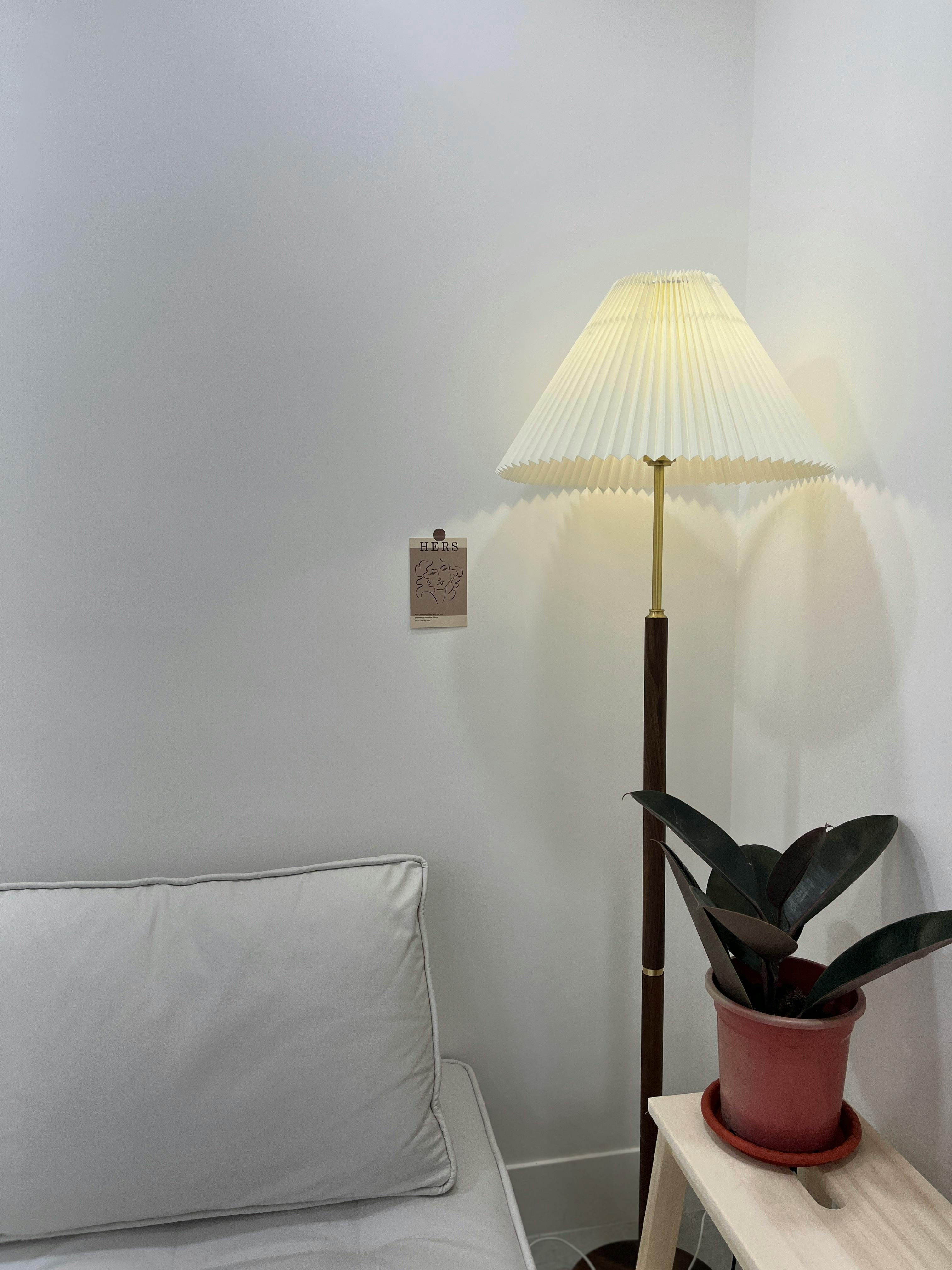 Free A cozy minimalist interior featuring a lamp, white wall, sofa, and potted plant. Stock Photo