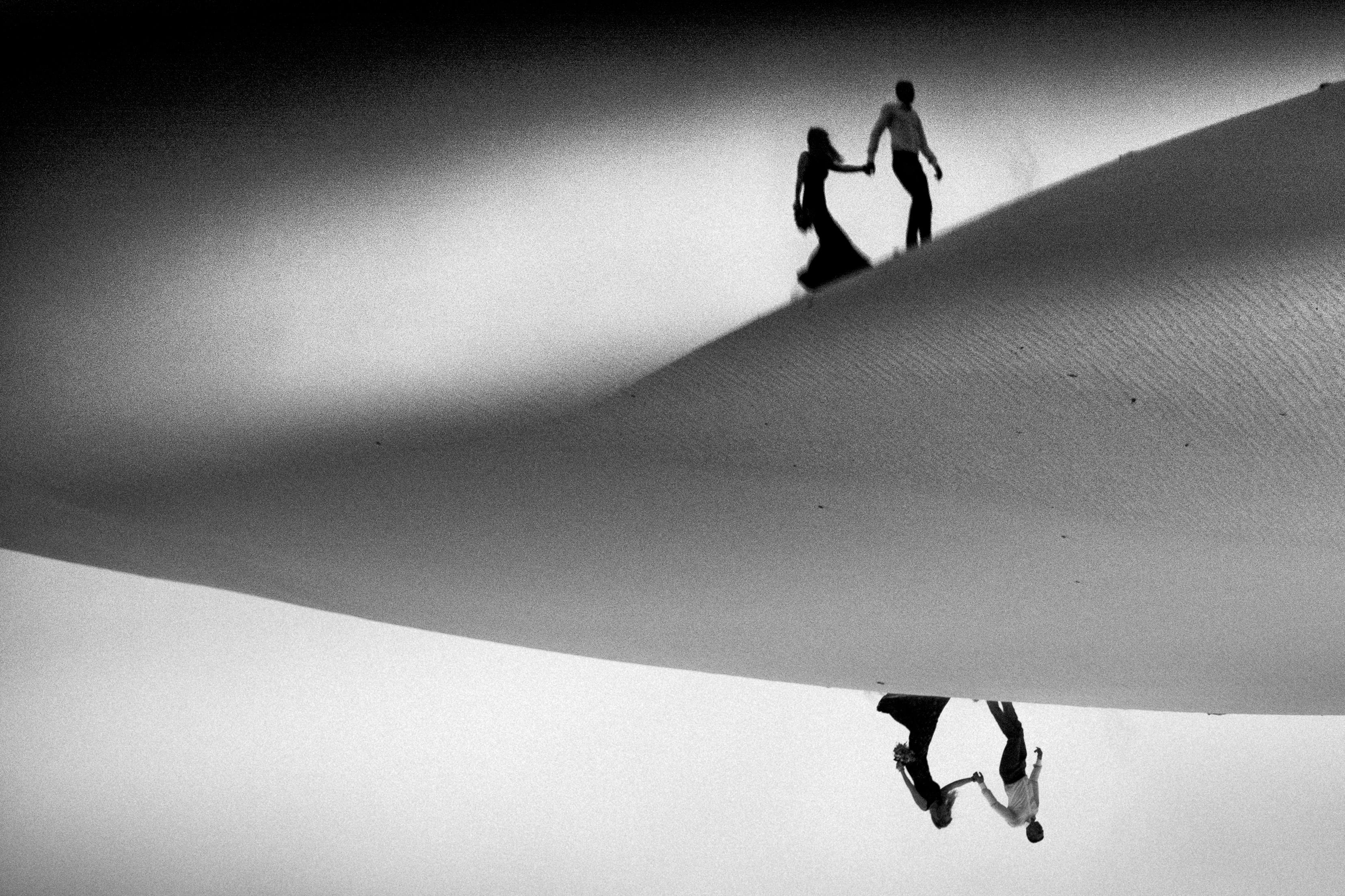 upside down and reflected photo of man and woman holding hands and walking through desert