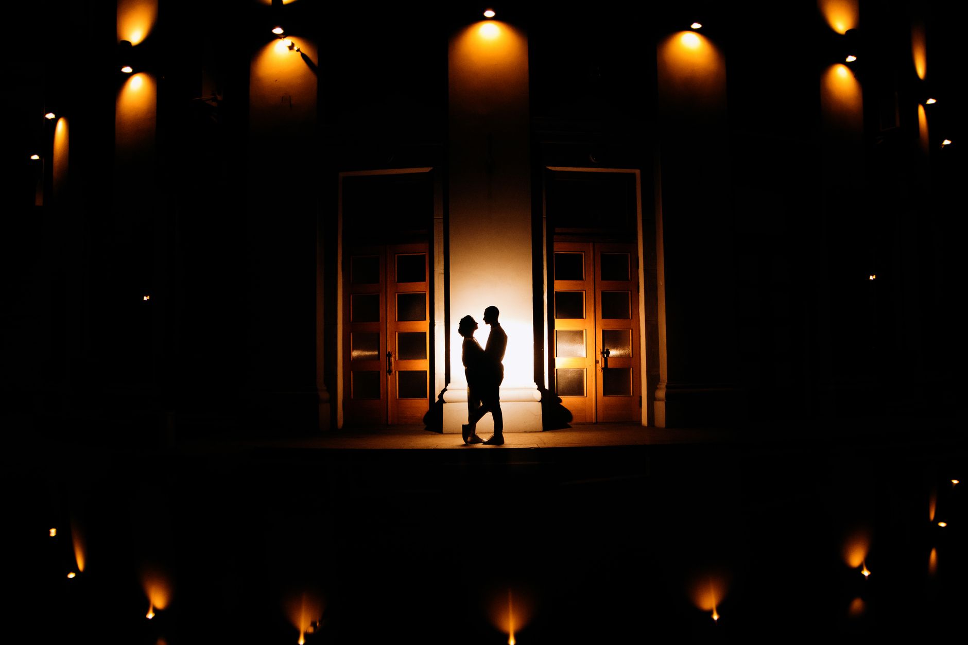 A romantic silhouette of a couple embraced under warm mood lighting outside at night.