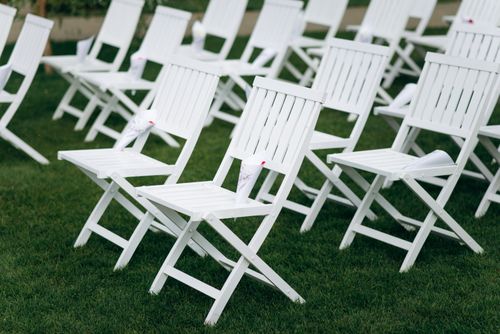 Free Rows of white folding chairs arranged neatly on a grassy field for an outdoor event. Stock Photo