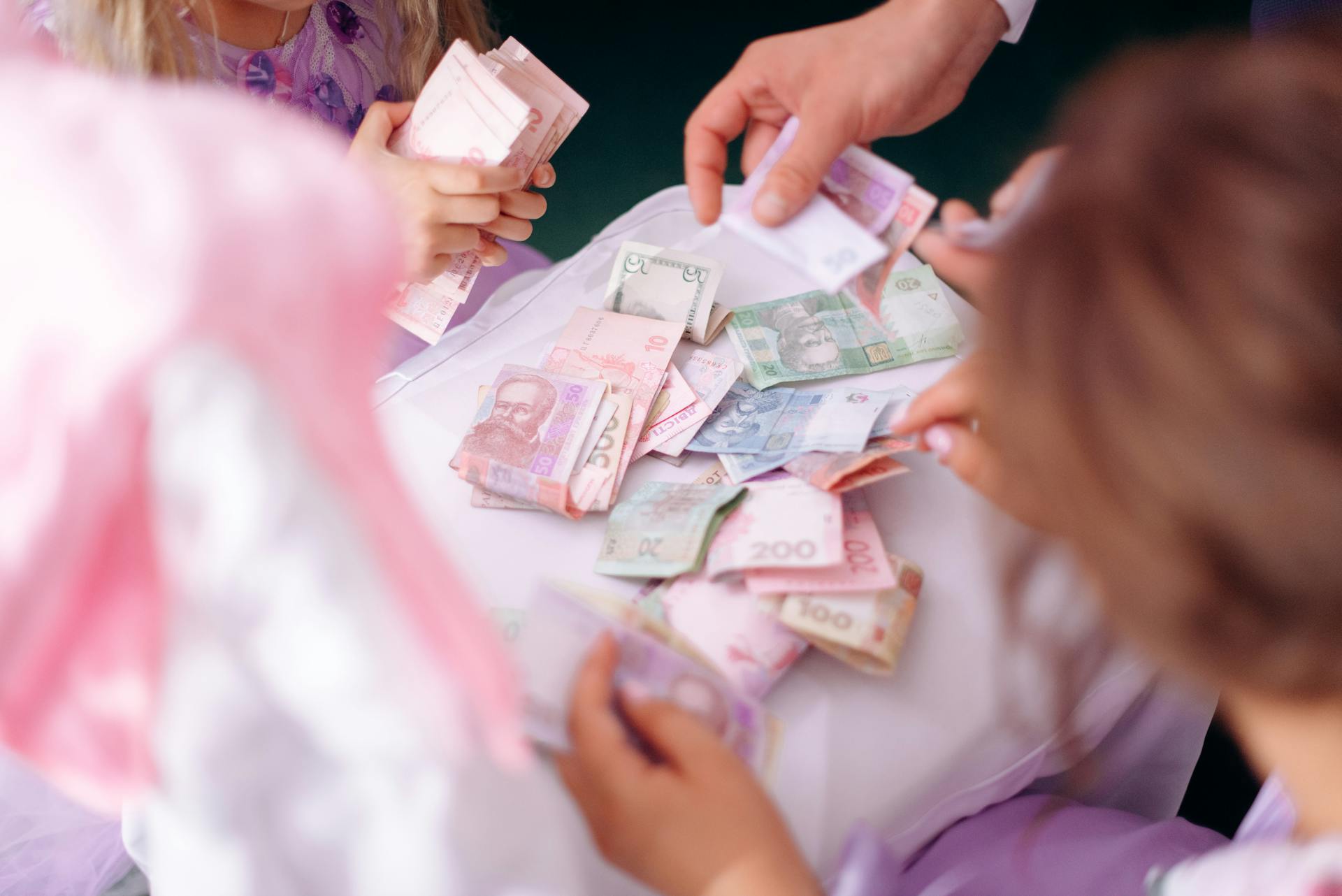 A child and adult hands sorting colorful banknotes on a table, symbolizing financial education.