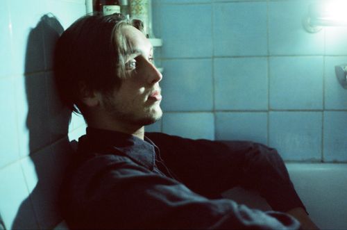 Free A young man sitting in a bathtub with a reflective expression, bathed in soft lighting. Stock Photo