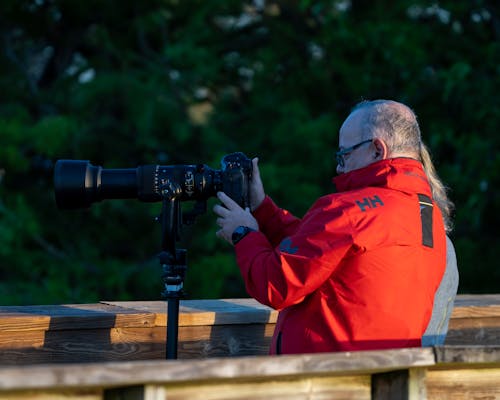 Man in Red Jacket Using Black Camera with Telephoto Lens