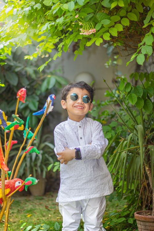 Free A cheerful child wearing sunglasses smiling in a lush garden setting. Stock Photo