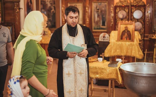 Man and a Child Standing next to a Priest in an Orthodox Church