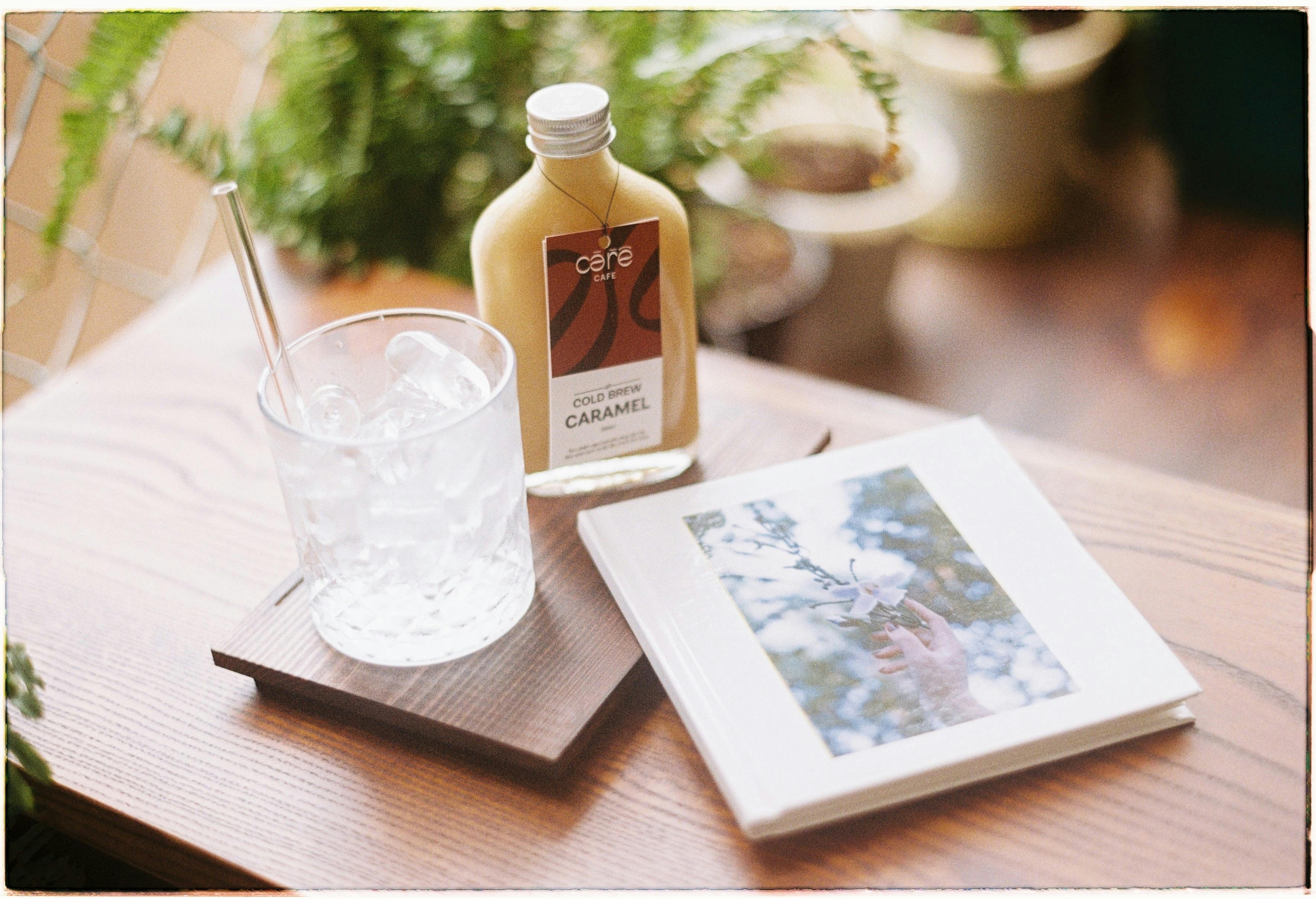 Glass of ice with caramel cold brew and photo book on wooden table.