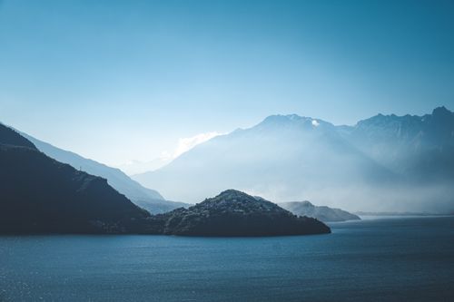 Free Serene landscape featuring a tranquil lake, misty mountains, and a clear blue sky, capturing the beauty of nature. Stock Photo