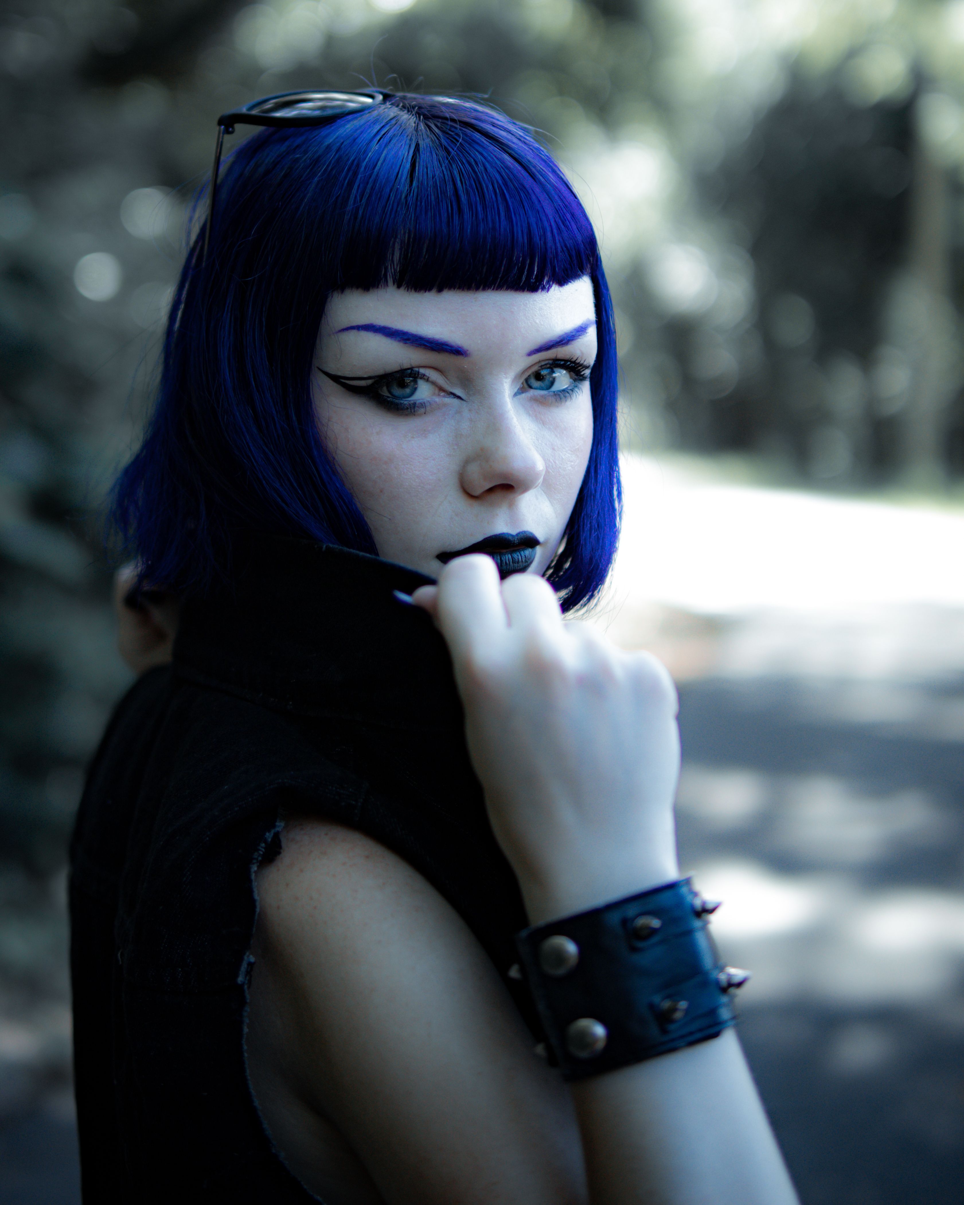 A striking portrait of a woman with blue hair and bold makeup, exuding confidence outdoors.