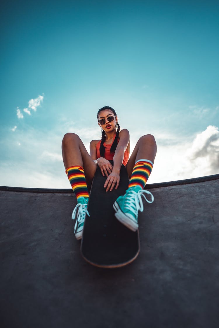 Girl Sitting On The Edge In Skatepark And Holding A Skateboard