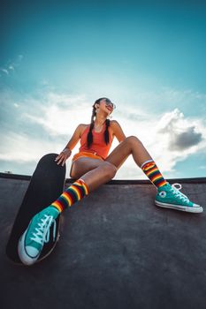 Young female skateboarder with colorful socks posing confidently at a skatepark on a sunny day.