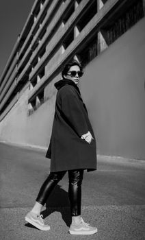A fashionable woman wearing sunglasses and coat in a Tehran street, captured in black and white.