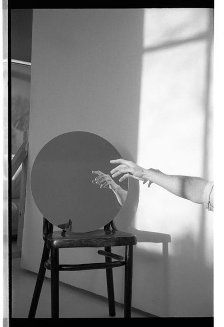 Black and white photo of a hand reaching for a reflection in a mirror on a chair.