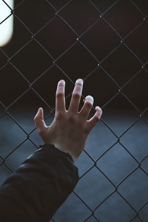 Free A close-up of a hand reaching through a chain link fence, conveying themes of longing and separation. Stock Photo