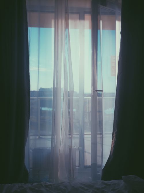 Free A peaceful view through sheer curtains to a balcony with soft natural light filtering in. Stock Photo