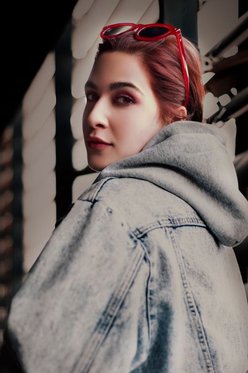 Free Stylish young woman wearing denim jacket and sunglasses, looking over her shoulder. Stock Photo