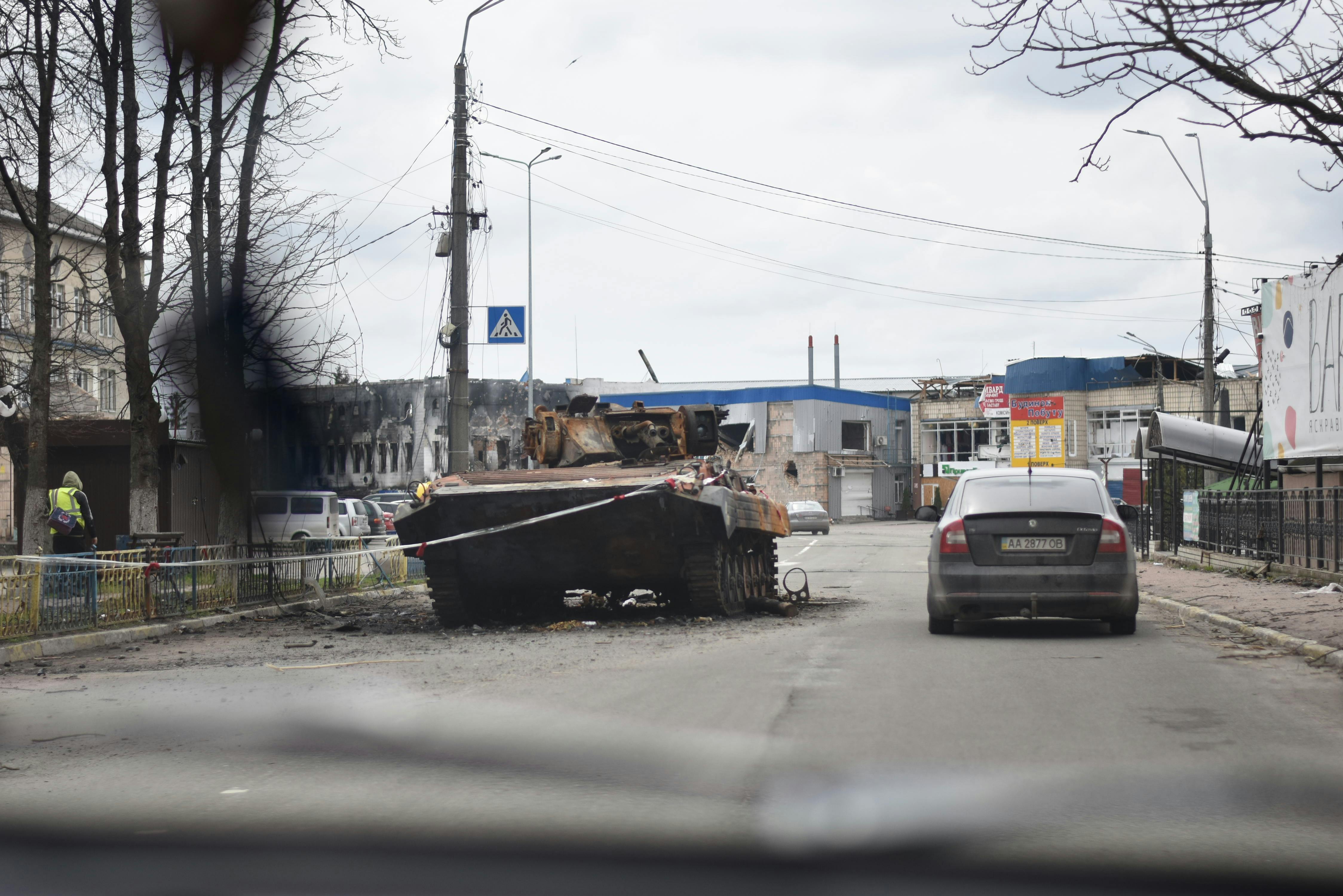 A military tank lies on an urban street amid debris with parked cars nearby.