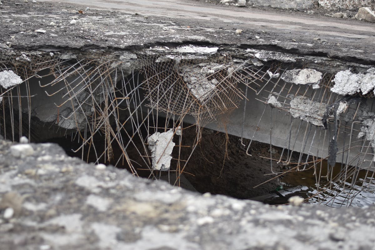Large pothole in road surface showing cracked pavement and standing water during spring thaw season