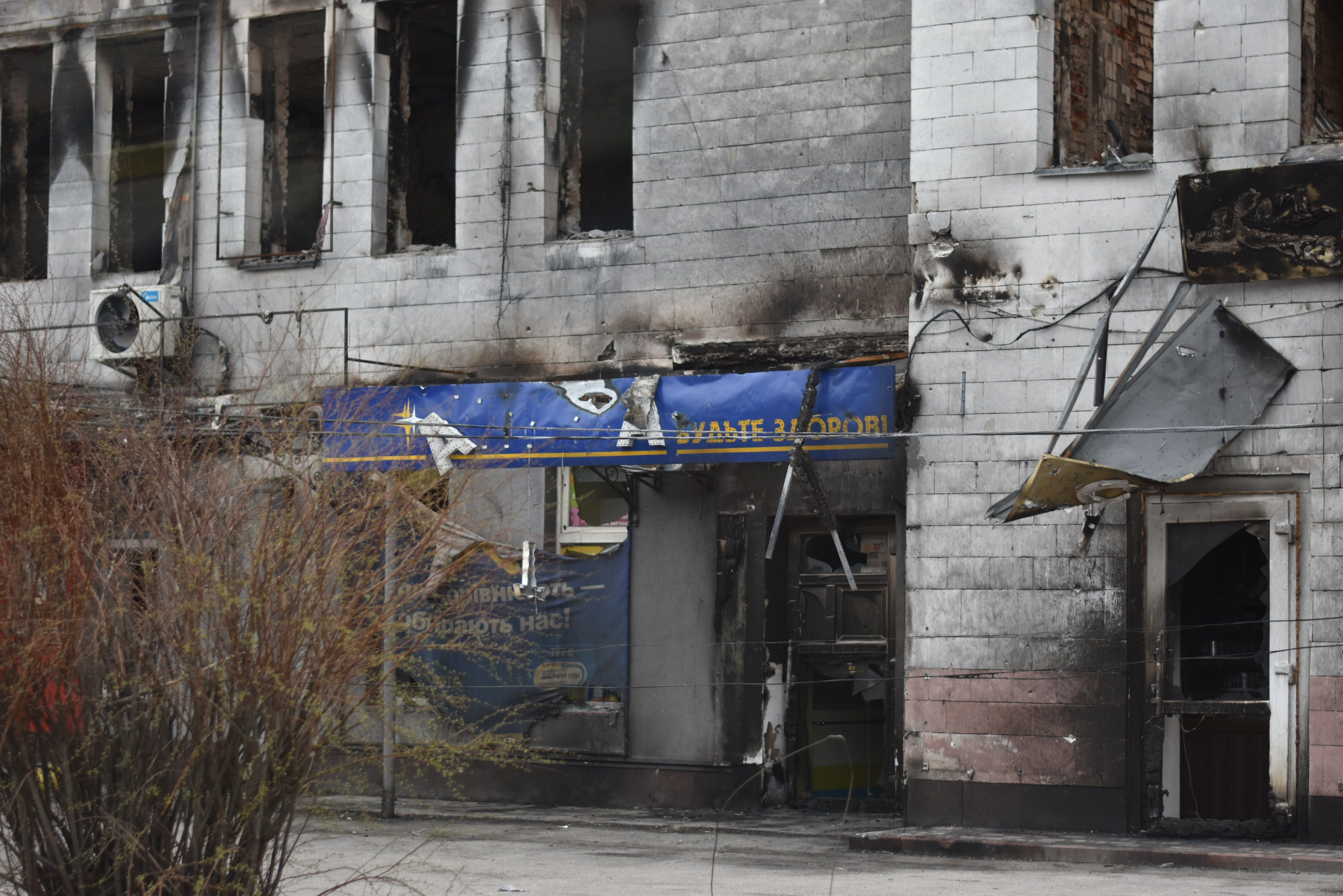 A fire-damaged multi-story building featuring a blue shop sign and broken windows in an urban setting.