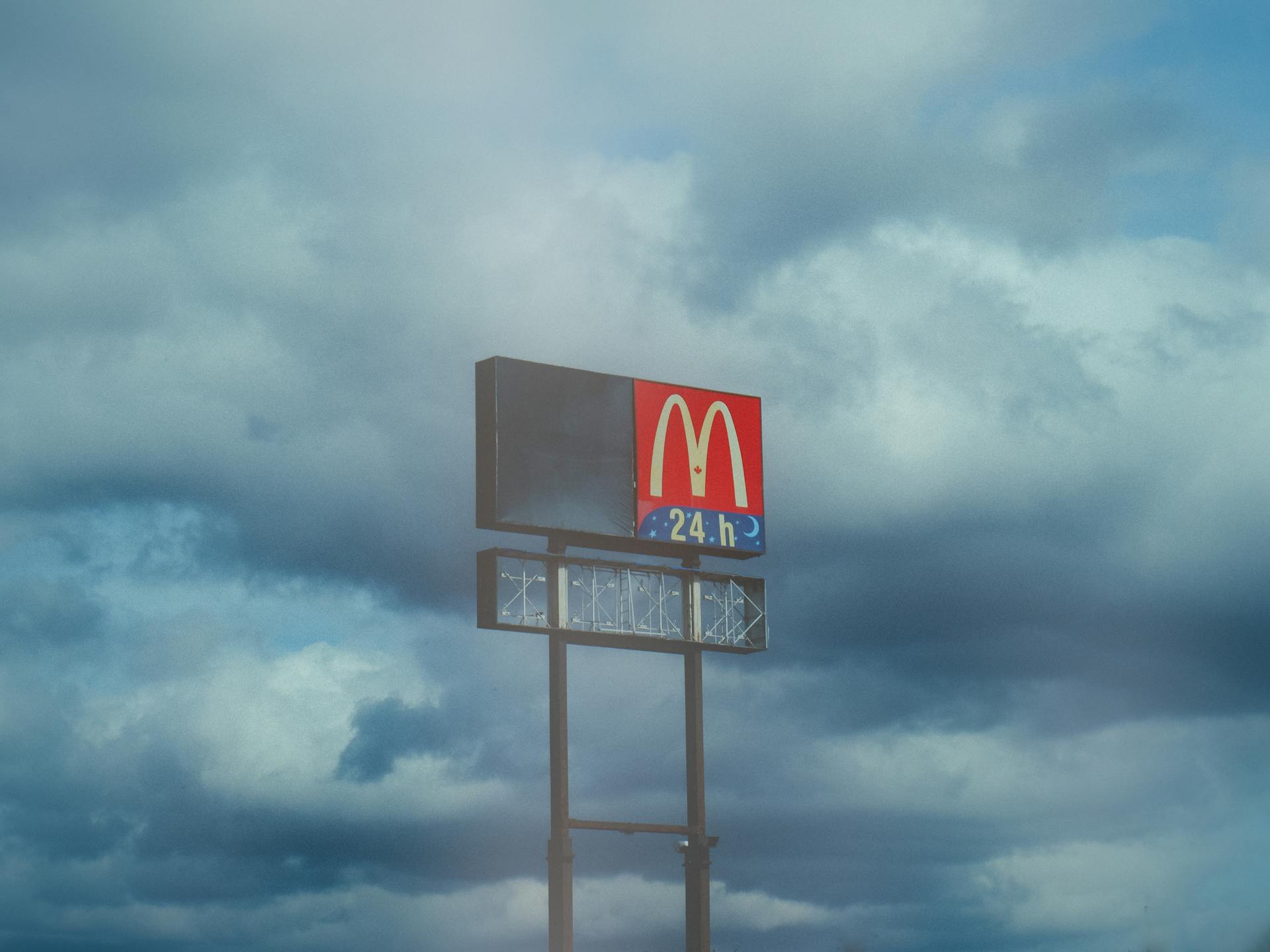 A McDonald's sign prominently stands against a dramatic cloudy sky, symbolizing fast food availability.