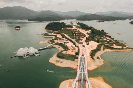 Stunning aerial view of Kenyir Lake with bridges and islands under cloudy skies.