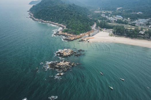 Stunning aerial shot of a serene beach, rocky coastline, and lush greenery meeting the deep blue sea.