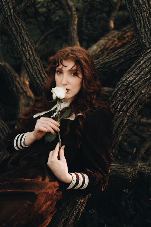 Redhead Girl in a Velvet Dress Holding White Rose in Forest 
