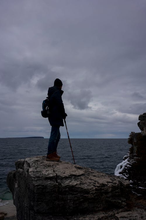Person Standing on Rock on Sea Shore under Clouds