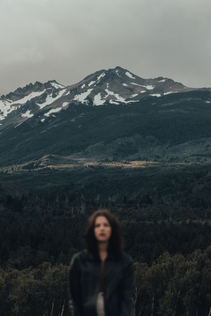 A moody winter mountain landscape with an out-of-focus woman in the foreground.