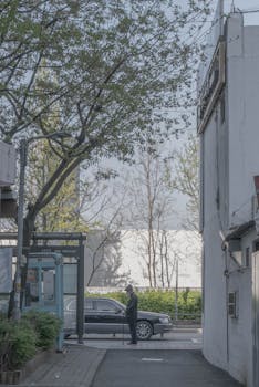 An elderly man with a walking stick waits at a bus stop in a quiet street in Seoul.