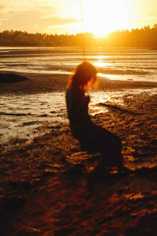 Silhouette of Woman Near Body of Water during Sunset