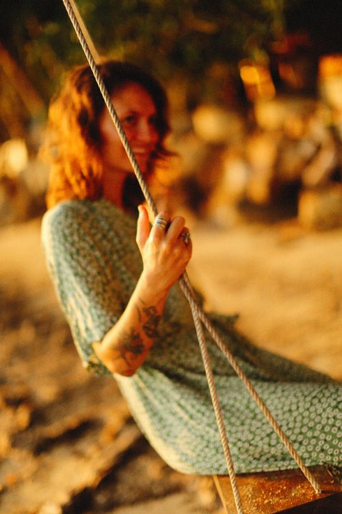 Free A woman joyfully swinging outdoors in a warm, serene setting with a blurred background. Stock Photo