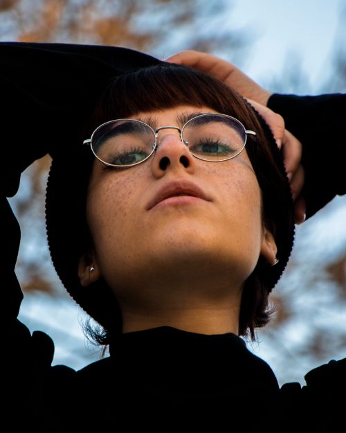Free A contemplative young woman with eyeglasses and freckles, looking up outdoors. Stock Photo
