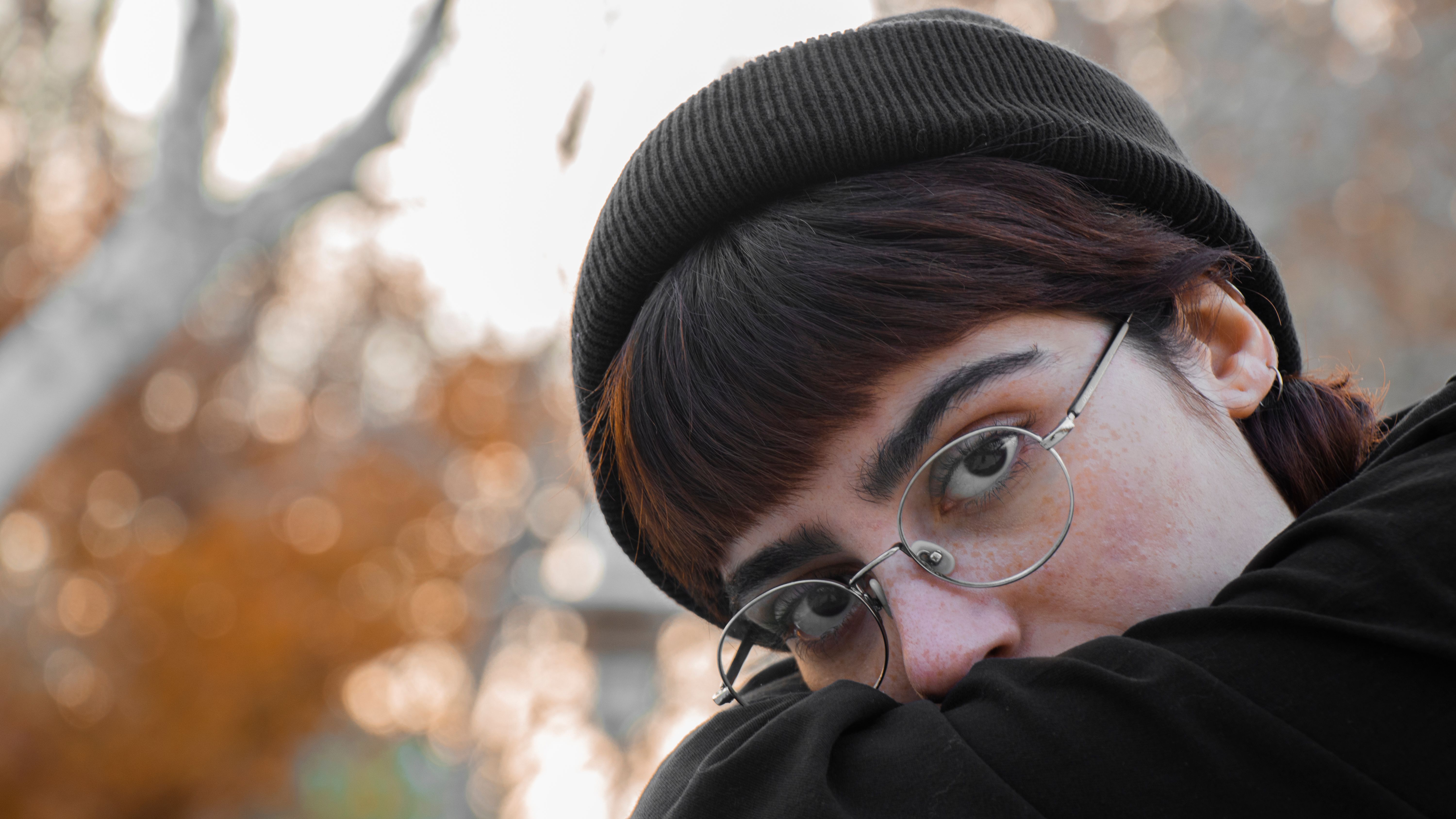 Captivating portrait of a woman with eyeglasses and beanie in an autumn setting.