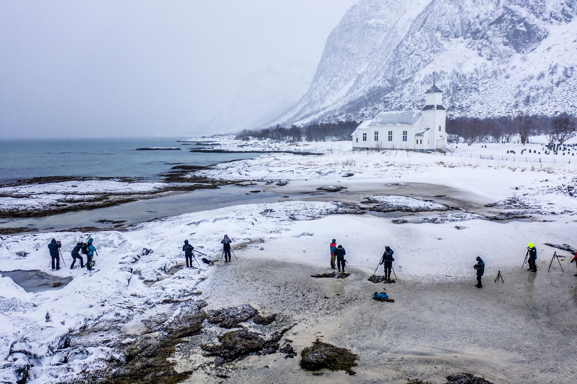 Photographers capture a snowy landscape with a church in Lofoten, Norway.