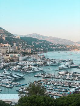 Aerial view of luxury yachts in Monaco's picturesque harbor with mountains in the background.