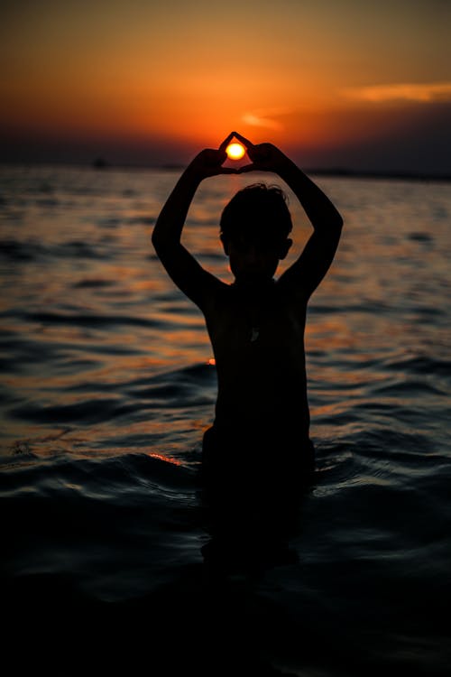 Silhouette of Boy in Water during Sunset