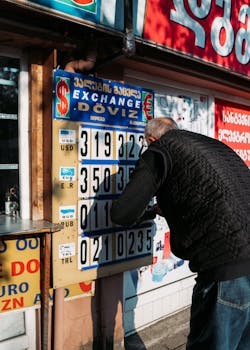 Man adjusting rates on a currency exchange board outside on a sunny day.