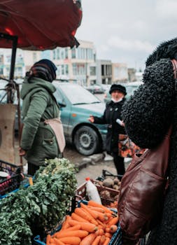 A vibrant street market scene with vendors and shoppers among fresh produce stalls.