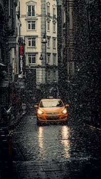 A yellow taxi drives through a rainy and dark cobblestone street in Istanbul, Turkey.