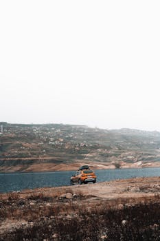 Yellow SUV parked by a serene lake with scenic hills in the background. Perfect for travel and nature themes.