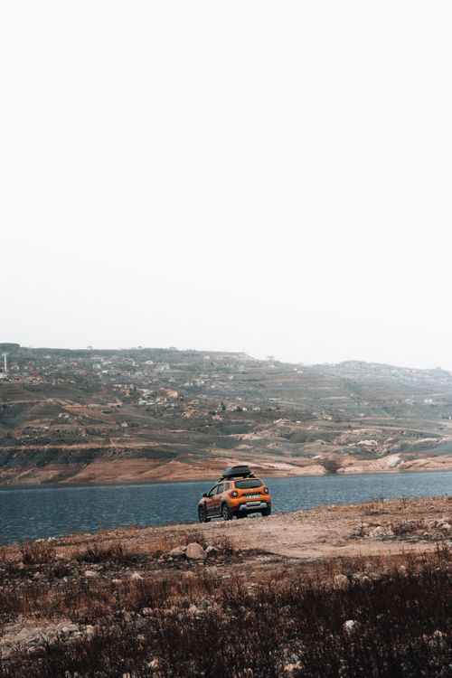 Free Yellow SUV parked by a serene lake with scenic hills in the background. Perfect for travel and nature themes. Stock Photo