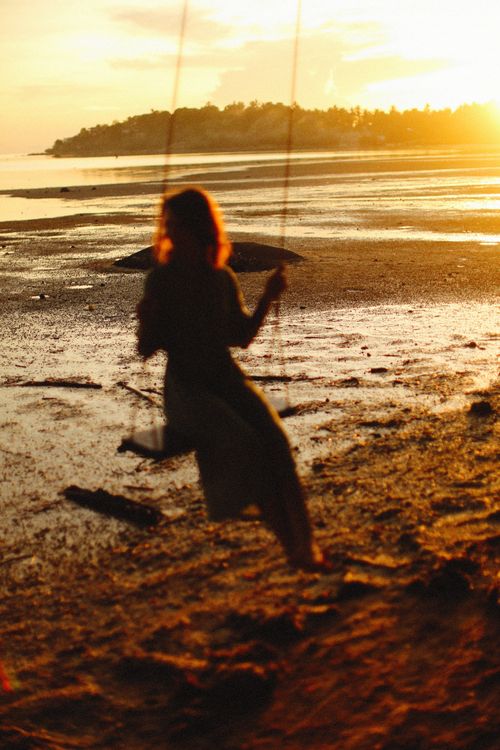 Free Silhouette of a woman on a swing by the beach at sunset, capturing a tranquil moment. Stock Photo