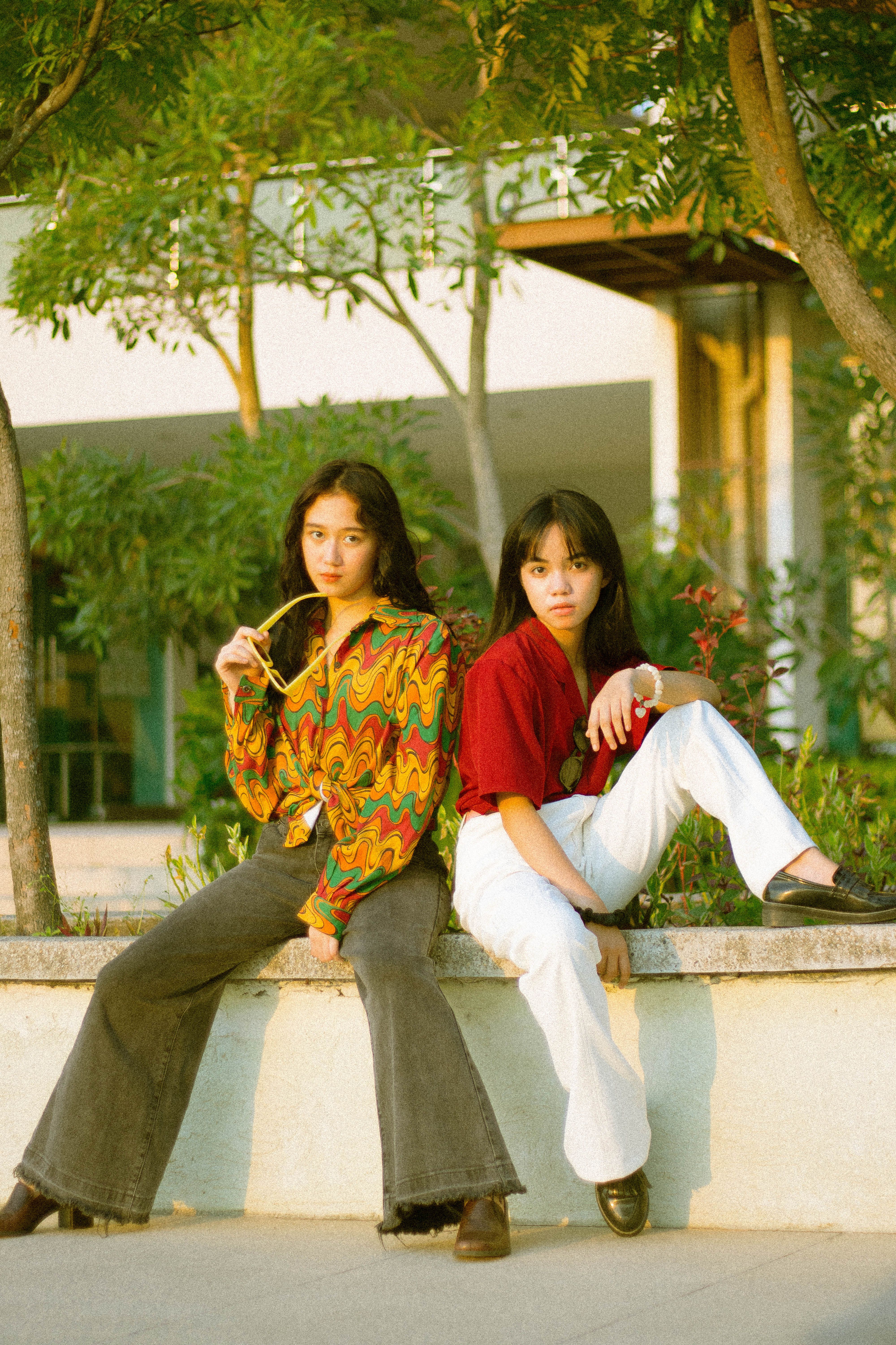Fotomural Chicas adolescentes con estilo sentadas en un banco, vistiendo atuendos vibrantes.